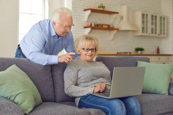 Sorridente coppia matura stare a casa con il computer portatile e comunicare o ordinare qualcosa online — Foto Stock