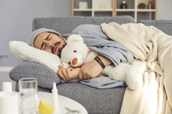 Fiatal boldogtalan férfi meleg ruhában alszik takaró alatt játékkal és fázással — Stock Fotó