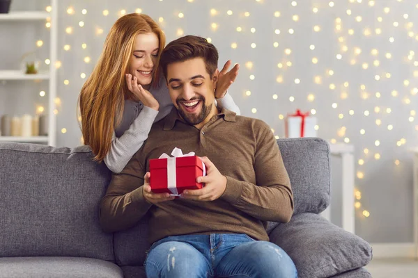 Radostně vzrušený muž sedí na pohovce v pokoji a dostává dárek od své přítelkyně. — Stock fotografie
