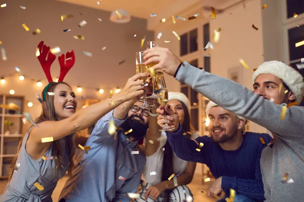 Grupo de jovens amigos positivos em chapéus decorativos celebrando o Natal com champanhe durante a festa — Fotografia de Stock