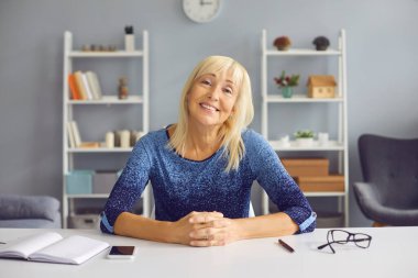 Çevrimiçi toplantı sırasında kameraya bakan gülümseyen orta yaşlı kadın.
