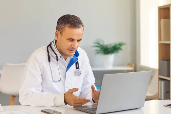 Arzt sitzt am Laptop, telefoniert mit dem Patienten und gibt medizinische Online-Beratung — Stockfoto