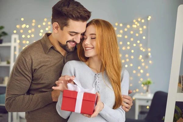 Joven pareja sonriente amorosa de pie, abrazando y abriendo la caja presente durante el día de San Valentín — Foto de Stock