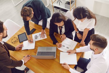 Satış ekibi ofis masasının etrafında toplanır, finansal verileri analiz eder ve dizüstü bilgisayarla evrak işlerini halleder.