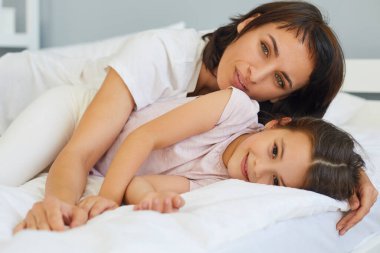 Genç anne yatak odasında küçük kızıyla oynaşıyor ve sarılıyor..