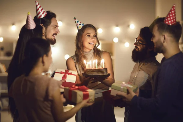 Ευτυχισμένη νεαρή γυναίκα κρατώντας την τούρτα γενεθλίων της και ευχαριστώντας τους φίλους για την έκπληξη και τα δώρα — Φωτογραφία Αρχείου