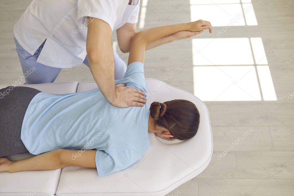 Hands of osteopath masseur doctor fixing lying woman patients back and shoulder