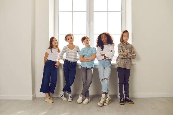 Des enfants sérieux et confiants debout par la fenêtre dans le hall de l'école ou du centre éducatif — Photo