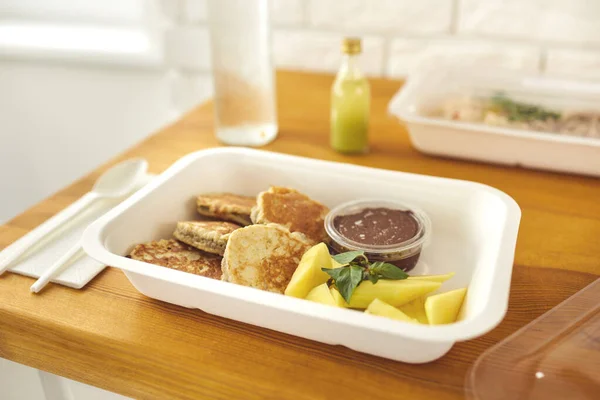 Gezonde heerlijke dessert van pannenkoeken met chocolade pudding en gesneden fruit in take-away container — Stockfoto