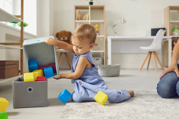 Anak kecil yang lucu berusia 2 tahun menempatkan mainan kembali di tempat mereka, membantu ibu untuk merapikan — Stok Foto