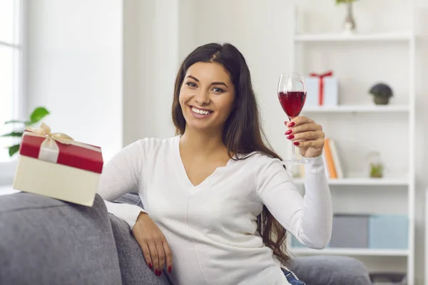 Mulher sentada em um sofá em casa levanta um copo de vinho na frente de uma webcam em uma data virtual. — Fotografia de Stock