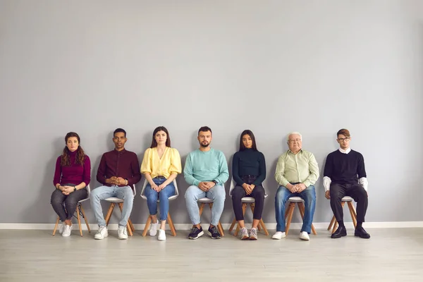 Multietniska personer som sitter i korridoren och väntar på sin tur för att träffa läkare eller för att få anställningsintervju — Stockfoto