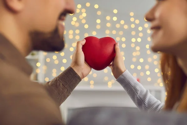 Primo piano del cuore rosso nelle mani di uomo e donna tenendolo sullo sfondo della parete con ghirlanda. — Foto Stock