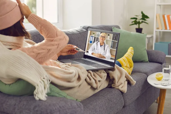 Ateşli bir kadın aile doktoruyla video görüşmesinde konuşuyor. Evdeki kanepede yatıyor.. — Stok fotoğraf