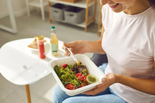 Smiling woman eating healthy balanced meal or salad in container delivered by food delivery service