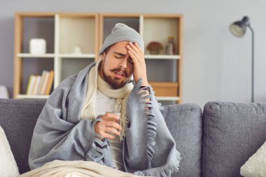 Şiddetli baş ağrısından muzdarip hasta bir adam gözleri ekose kumaşa sarılmış olarak oturur..