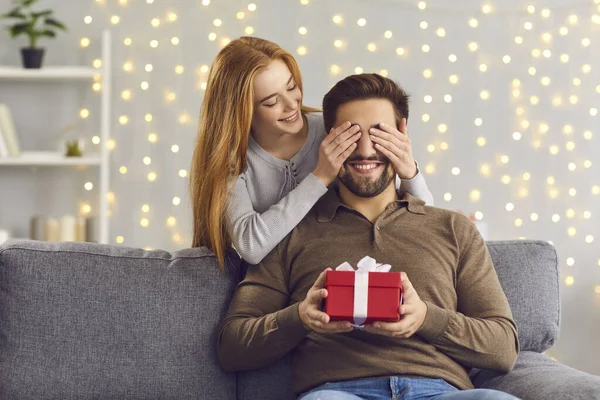 Usmívající se mladá žena zakrývá své milence oči a dává mu překvapení dárek — Stock fotografie