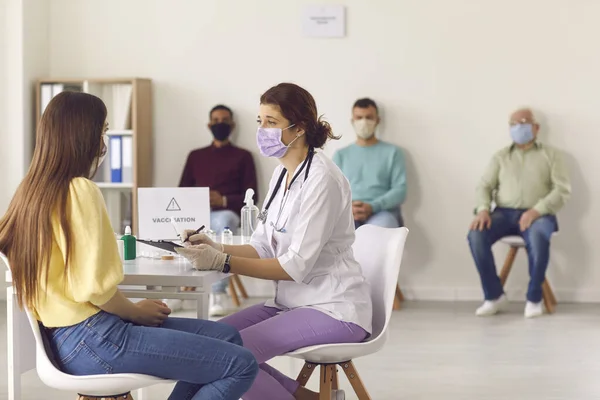 Doctor in face mask interviewing young woman before giving her antiviral vaccine — Stock Photo, Image