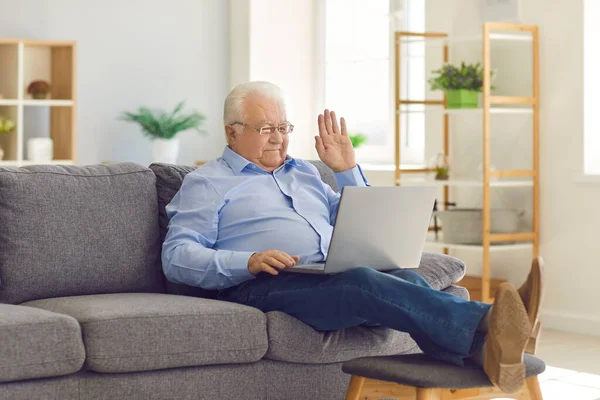 Heureux homme âgé souriant assis sur le canapé et parlant sur appel vidéo avec la famille à l'aide d'un ordinateur portable. — Photo