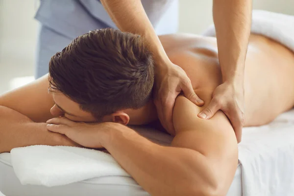 Jovem cliente do sexo masculino desfrutando de massagem corporal relaxante no moderno centro de bem-estar ou saúde — Fotografia de Stock