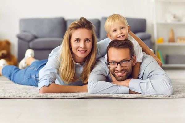Feliz familia joven relajándose en la alfombra caliente en la sala de estar de su casa recién comprada — Foto de Stock