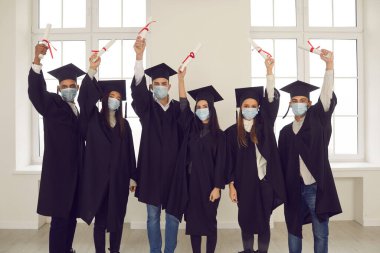 Üniversite mezunları koruyucu tıbbi yüz maskeleri takıyor ve diplomaları var.