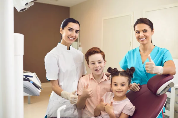 Стоматологічна клініка. Усміхнений стоматолог, медсестра та діти хлопчик і дівчинка дивляться на камеру під час візиту — стокове фото