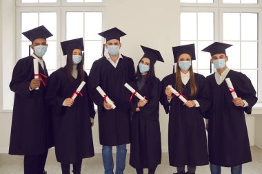 Çok ırklı üniversite mezunlarının grup portresi diplomalarını elinde maskelerle