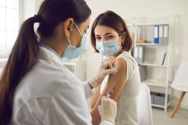 Young woman in face mask getting coronavirus or flu antiviral vaccine at the hospital