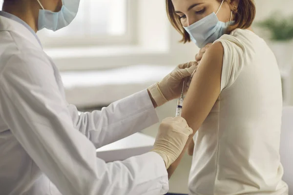 Young woman in face mask getting Covid-19 or flu antiviral vaccine at doctors office — Stock Photo, Image