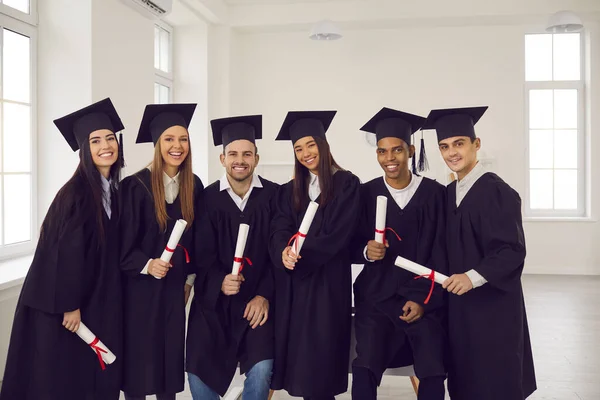 Group of young happy university graduates multiethnic friends with diplomas in hands