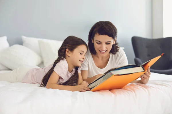 Ibu dan anak yang bahagia berbaring bersama di tempat tidur dan membaca buku — Stok Foto