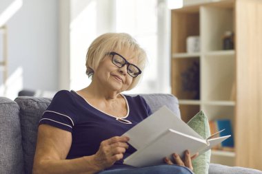 Gülümseyen kadın oturma odasındaki kanepede otururken defterin sayfalarını karıştırıyor..