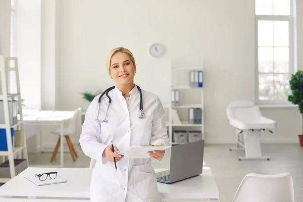 Porträt einer stilvollen Ärztin mit Dokumenten in der Hand in der Nähe ihres Arbeitsplatzes. — Stockfoto