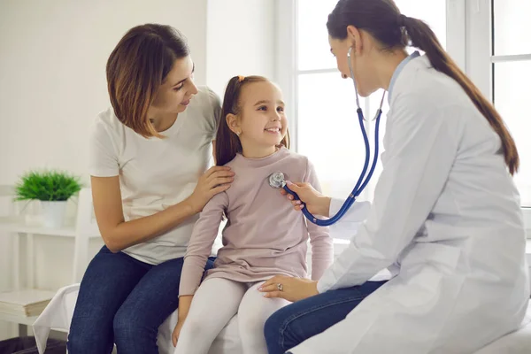 Joven pediatra sonriente usando estetoscopio para revisar a la niña sonriente —  Fotos de Stock