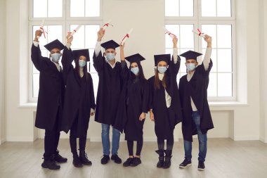 Birçok başarılı üniversite mezunu diplomalarını elinde tutan maskeli kişiler.