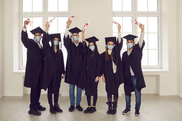Ομάδα επιτυχημένων πτυχιούχων πανεπιστημίου με μάσκες προσώπου που κρατούν τα πτυχία τους — Φωτογραφία Αρχείου