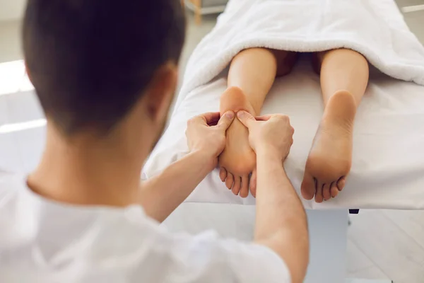 Man masseur doctor in white uniform massaging lying patients heels