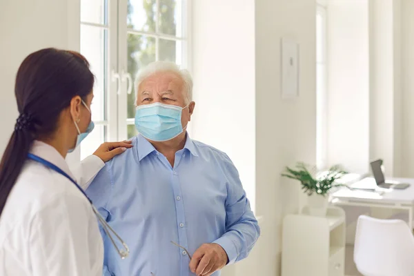 Kobieta lekarz dotykając ramię dojrzały starszy mężczyzna pacjent w masce po wizycie w klinice — Zdjęcie stockowe