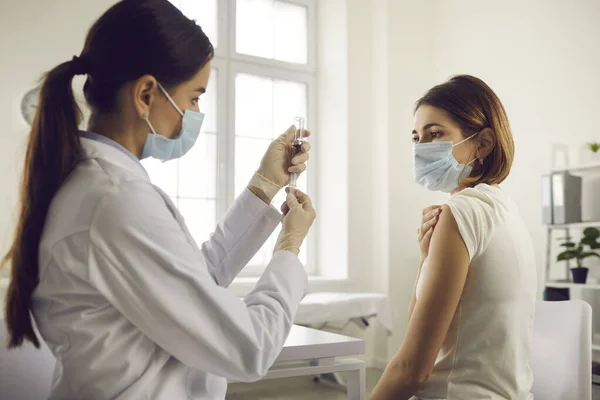 Медсестра витягує ліки з флакона перед введенням противірусної вакцини молодій жінці — стокове фото