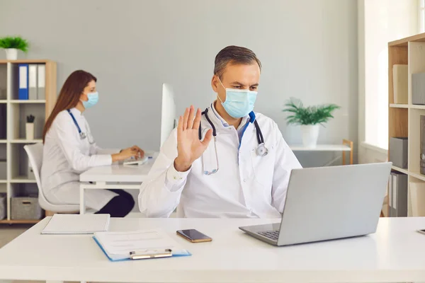 Middle aged man doctor in protective medical mask communicating online with patient — Stock Photo, Image