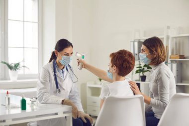 Küçük çocuk hastanede eğleniyor ve doktor sıcaklığını silah termometresiyle ölçüyor.
