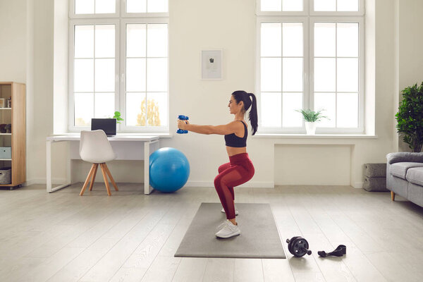 Profile view of a slender athletic woman training with dumbbells holding them in front of her.
