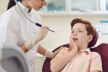 Çocuk diş kliniği. Küçük çocuk dişçi koltuğunda oturuyor ve şiddetli diş ağrısı çekiyor..
