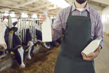Çiftlikte cam şişeler dolusu taze organik süt taşıyan bir erkek çiftçinin kırpılmış görüntüsü..