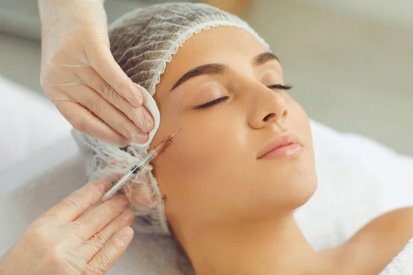 Serene woman getting beauty botox anti-aging injection to cheek from professional cosmetologist — Stock fotografie