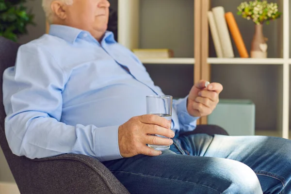 Senior man met glas water het nemen van voorgeschreven pillen zitten in een fauteuil thuis — Stockfoto