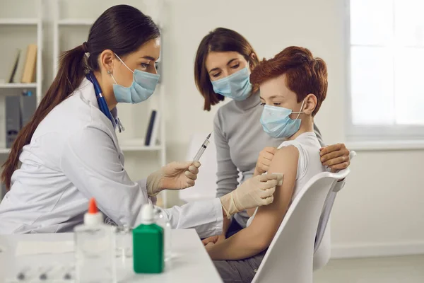 Жінка-педіатр в медичній захисній масці протирає руку пацієнта підлітка перед вакцинацією — стокове фото
