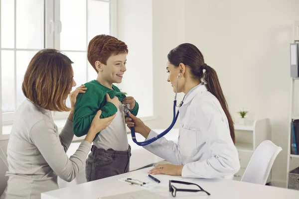 Doutor ouve com um estetoscópio para um menino que veio com sua mãe para um exame médico. — Fotografia de Stock
