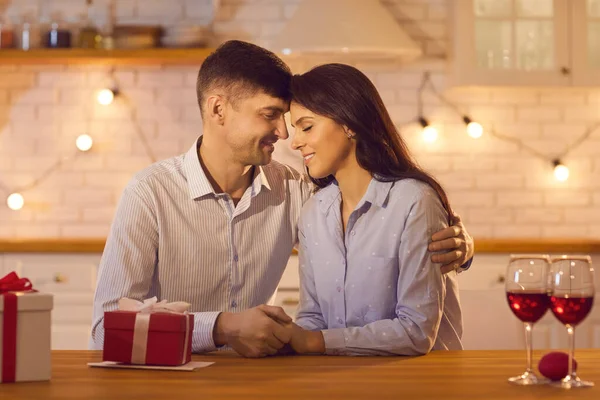 Jovem casal amoroso sentado à mesa com vinho e presentes de férias, abraçando e celebrando o dia dos namorados — Fotografia de Stock